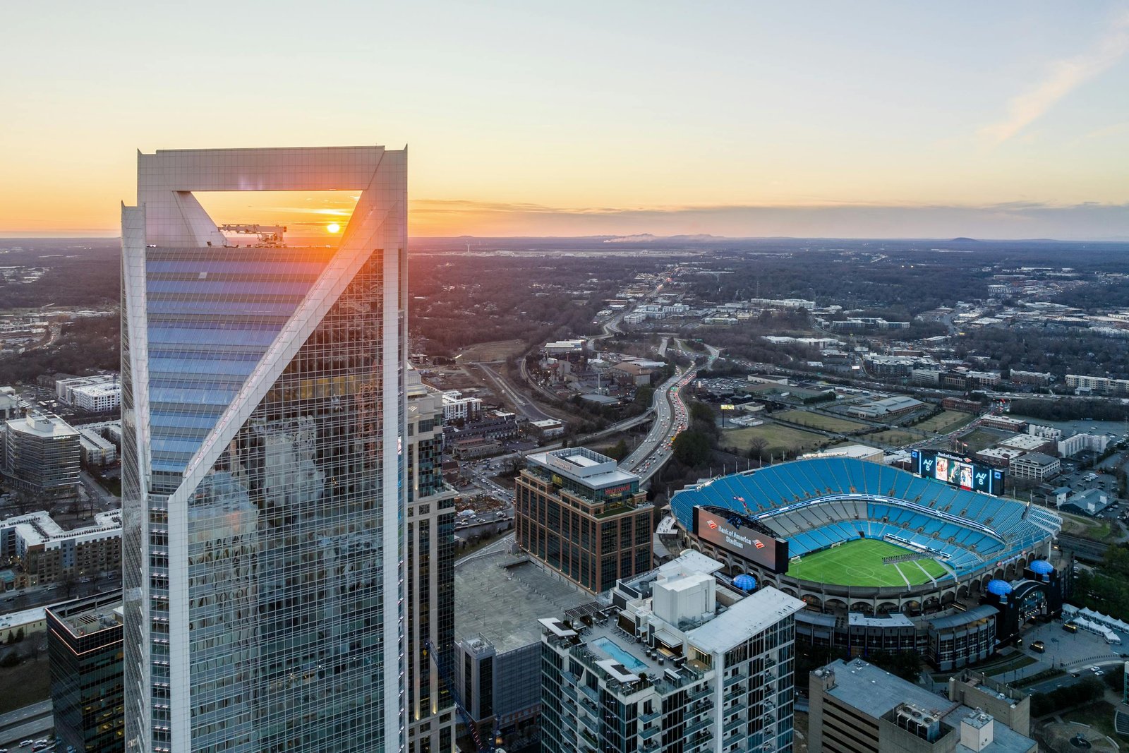 Aerial view of Charlotte's skyline and Bank of America Stadium during vibrant sunset.