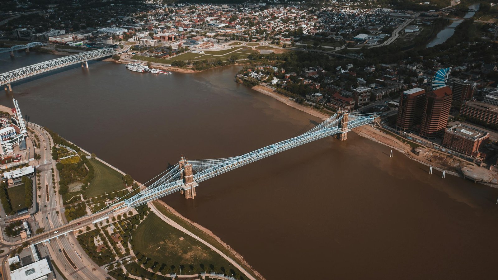 From above of city view and John Roebling Suspension Bridge crossing river with muddy water located in USA