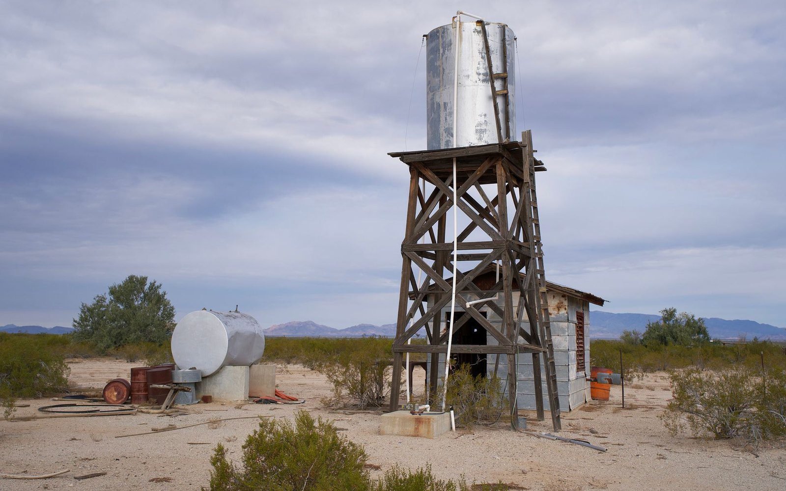 Elevated steel water tank on a wooden tower beside a storage tank on rural Arizona desert land