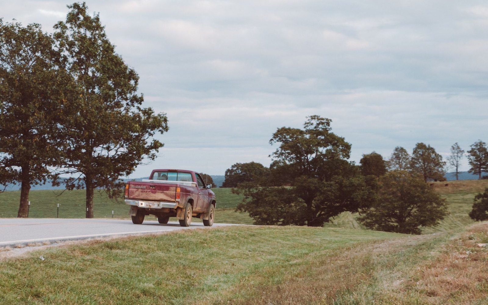 Pickup truck on a two-lane county road through Arkansas pasture and oak trees