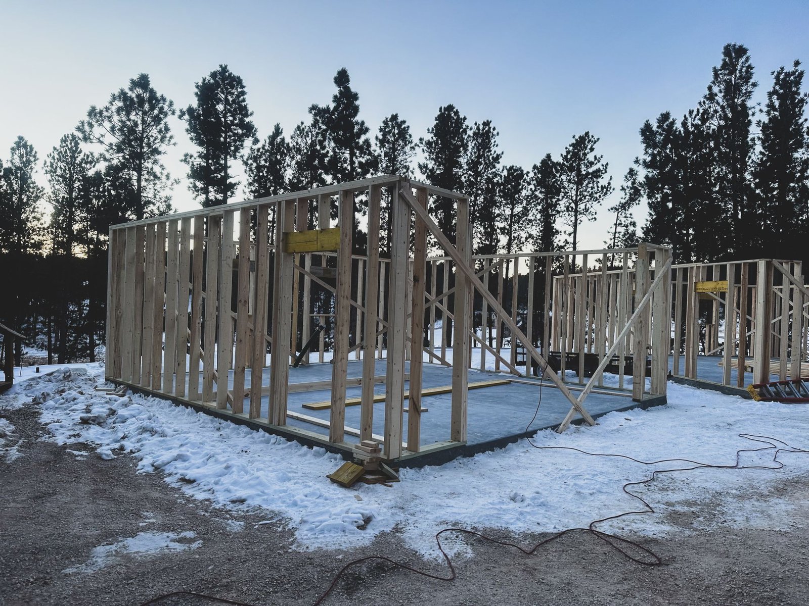 Wood framing of homes under construction on a snowy lot among pine trees