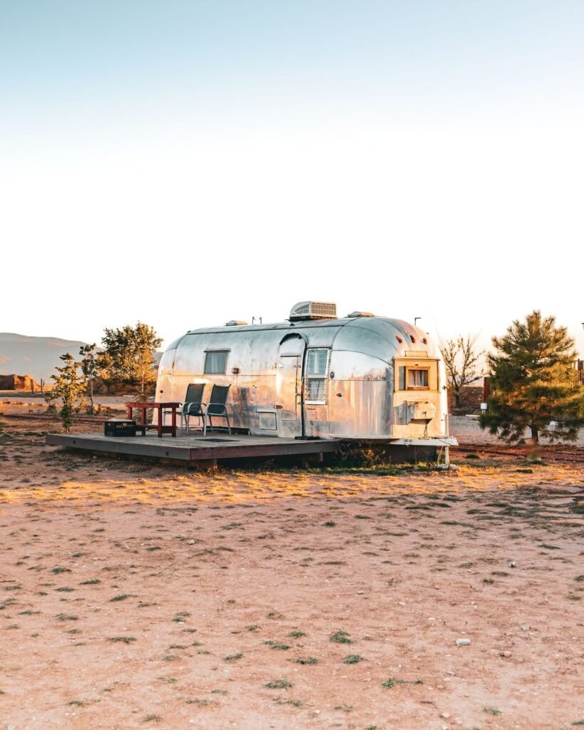 A vintage Airstream travel trailer on a wooden deck in the high desert near Taos, New Mexico, with trees behind it