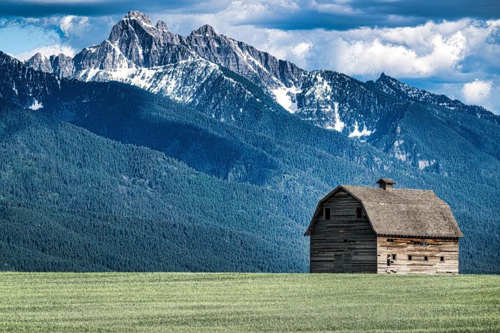 Weathered wooden barn on green pasture below the snow-capped Mission Range near Ronan, Montana